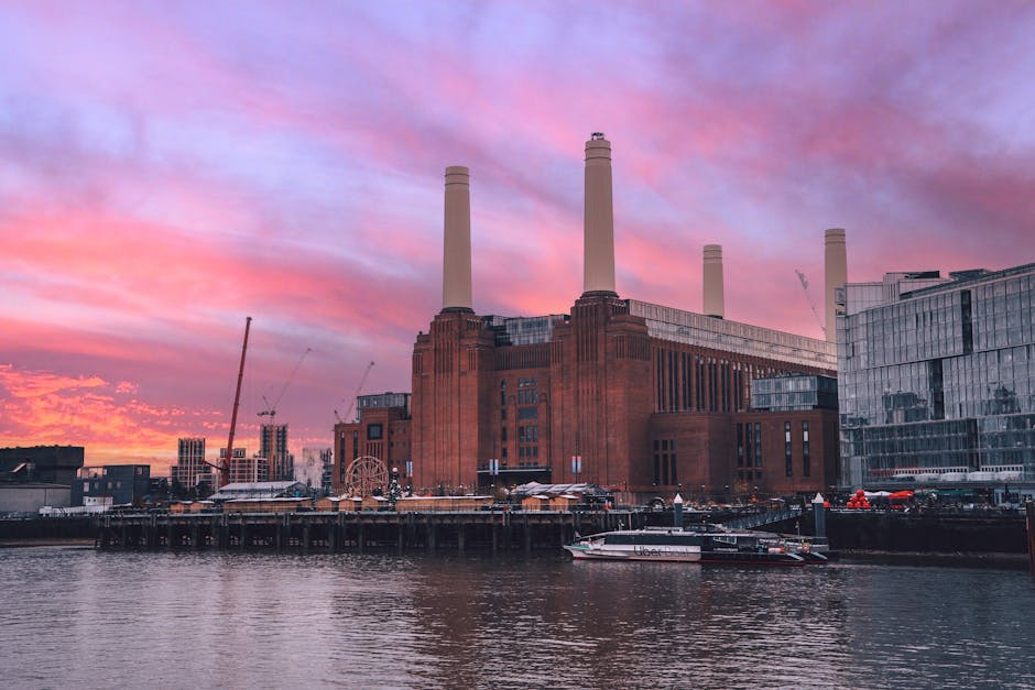 A close-up view of the iconic Battersea Power Station's two large, cylindrical chimney stacks made of beige-colored material with vertical ridges, set against a clear blue sky during daytime. The lowe