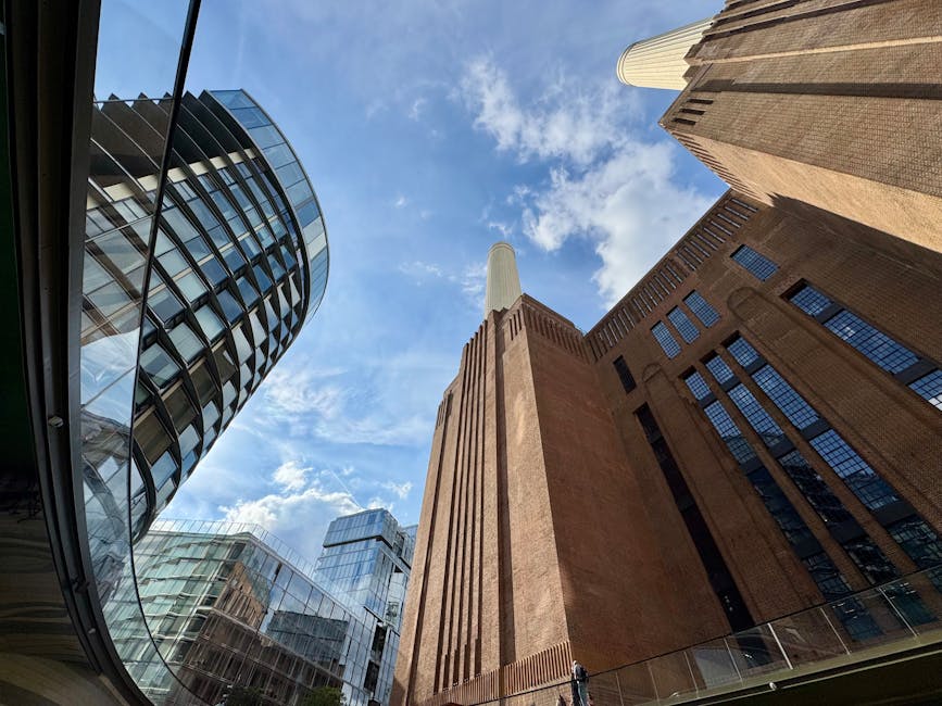 A wide-angle view of tall modern and historic buildings from ground level, with the sky visible overhead featuring scattered white clouds. On the left, a contemporary glass-clad skyscraper with curved
